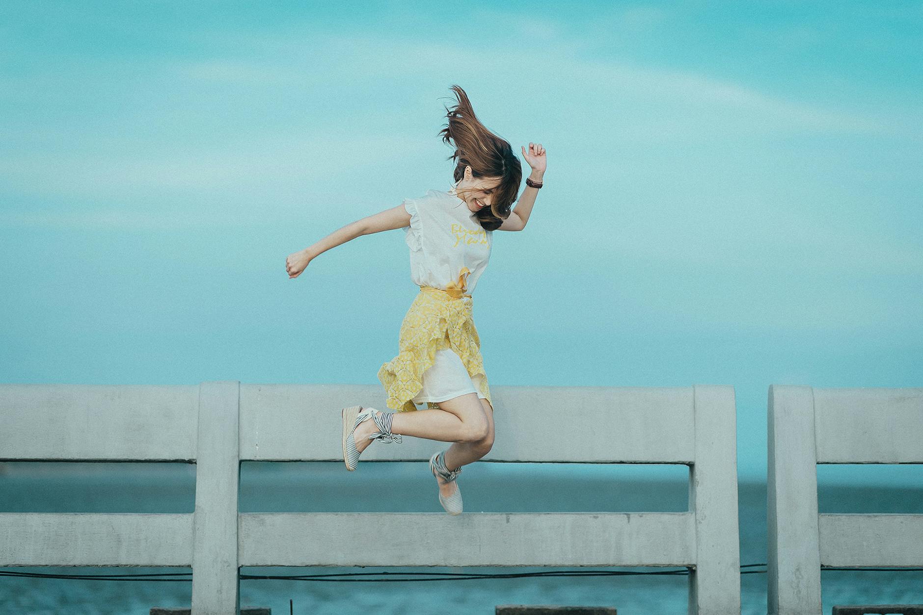 jumpshot photography of woman in white and yellow dress near body of water