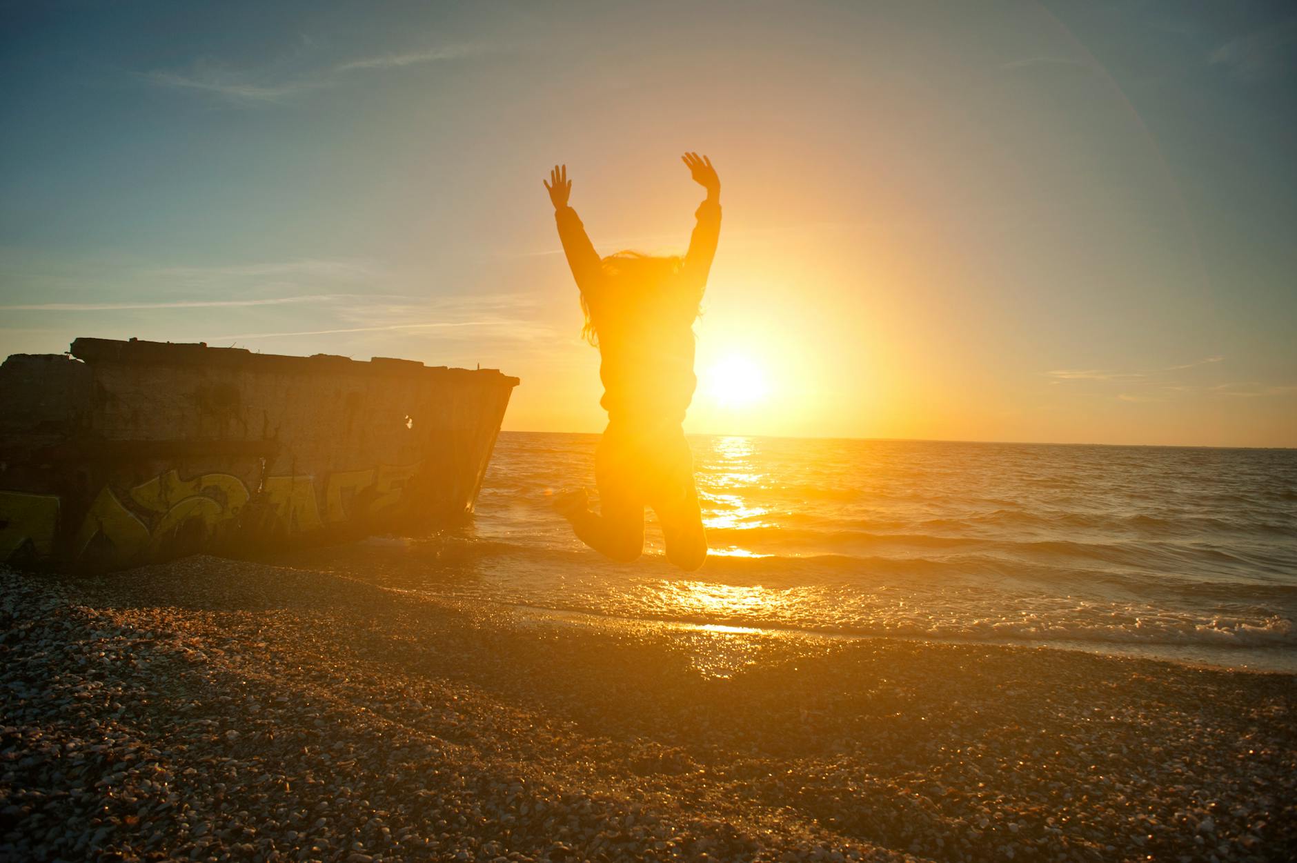 person jumping on seashore during golden hour