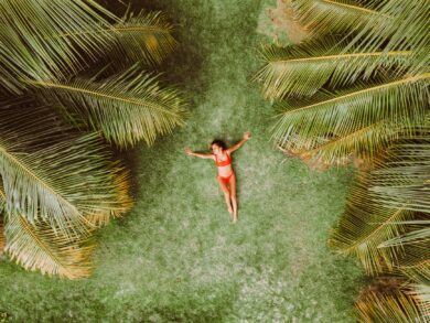 woman lying on green grass among palms at resort