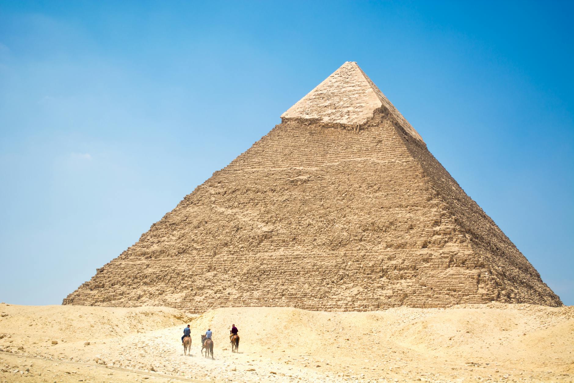 people riding a camel near pyramid under blue sky