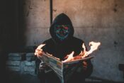 person with black mask holding a burning news paper