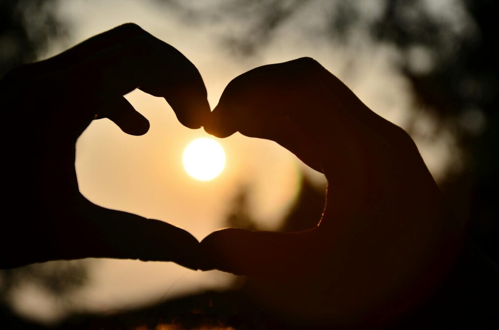 silhouette of person hand doing heart shape during sunset